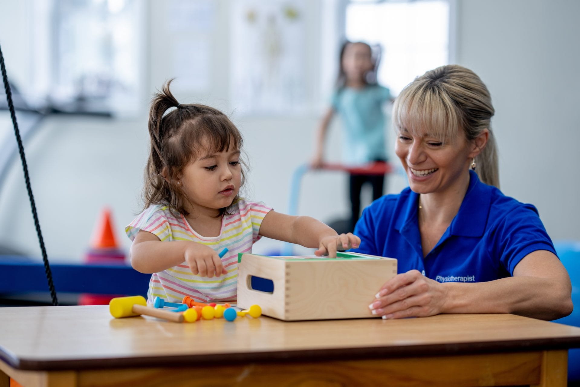 Teacher and young girl smiling while playing with blocks in a classroom.