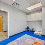 Small therapy room with bright floor mat, window view, and open doorway to hallway.