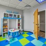 Therapy space with cube shelving unit, toys, and green-and-blue foam flooring.