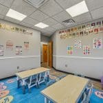 Therapy classroom with blue flooring, small desks, and educational posters on walls.