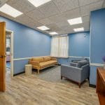 Clinic reception area with blue walls, wood flooring, front desk, and gray seating for visitors.