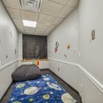 Compact therapy room with cushioned mat seating and neutral walls.