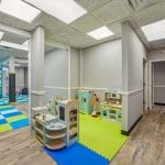 Indoor therapy gym with padded columns, climbing wall, and blue-and-green checkered floor mats.