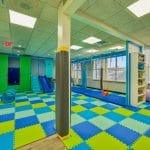 Sensory gym area with suspended equipment, foam flooring, and padded support beams.