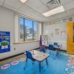 Child therapy space with wall decorations, bright rug, activity table, and wooden door to hallway.